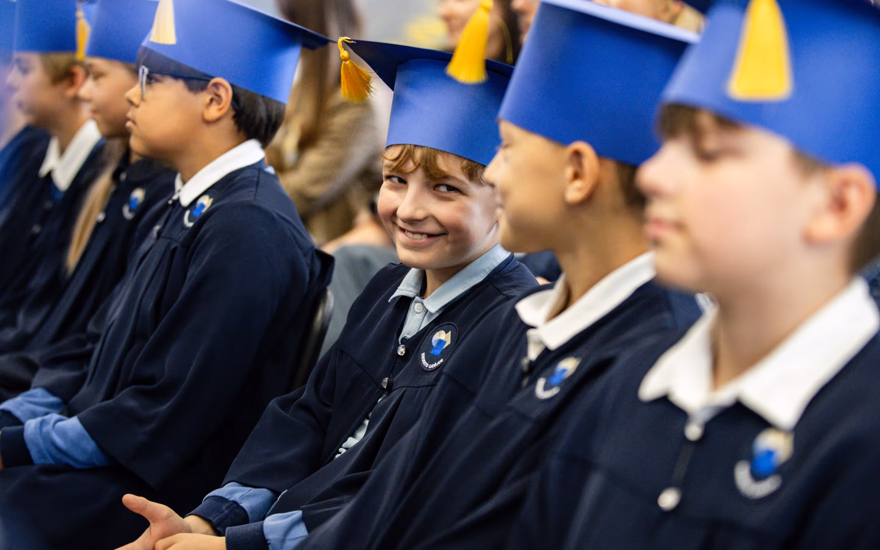 Erudito Lyceum students in navy graduation gowns and gold-tasseled caps, one smiling at the camera.