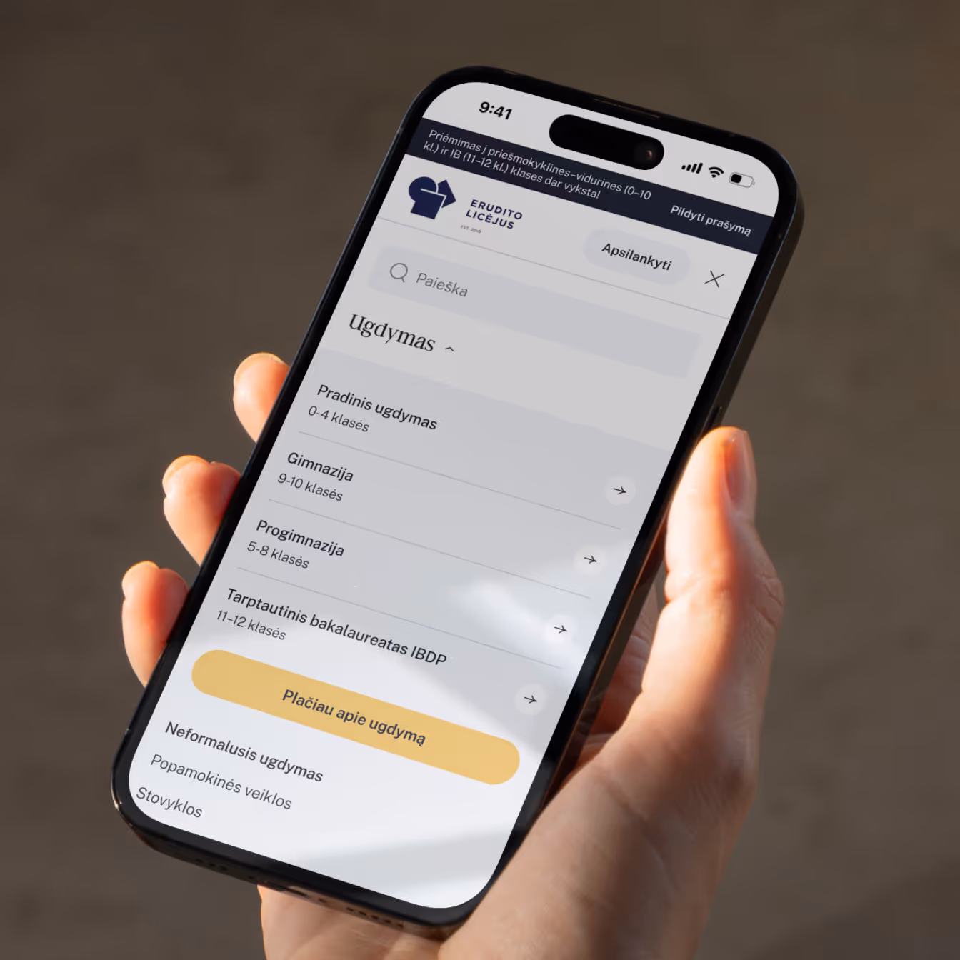 A hand holding a phone with Erudito Lyceum's mobile site open - admissions banner, search and menu.